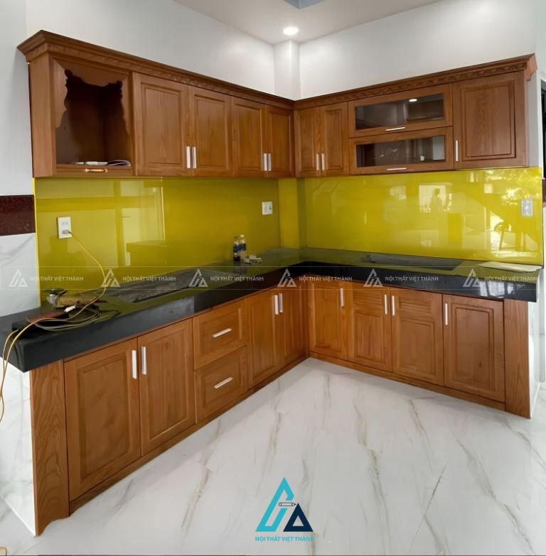 Tủ bếp gỗ tự nhiên chữ L phối kính ốp tường màu vàng nổi bật