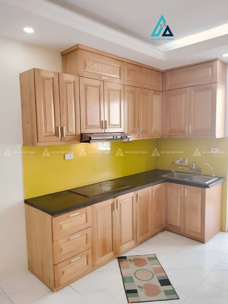 Tủ bếp gỗ chữ L phối kính ốp tường vàng nổi bật cho gia đình